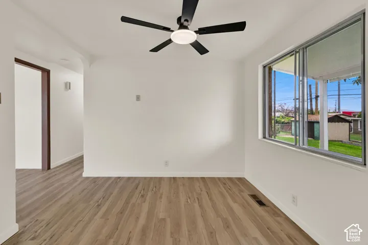 Bright and spacious room featuring New wood-finish flooring throughout, large picture window with natural light and outdoor visibility, and New modern ceiling fan with integrated lighting fixture