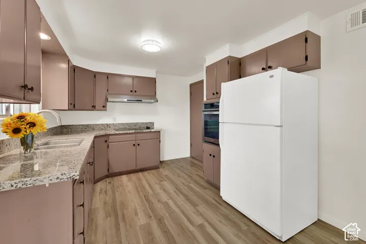 Kitchen featuring New LVP  wood-finish flooring, built-in cabinetry, granite-style countertops, stainless steel sink, and a built-in oven