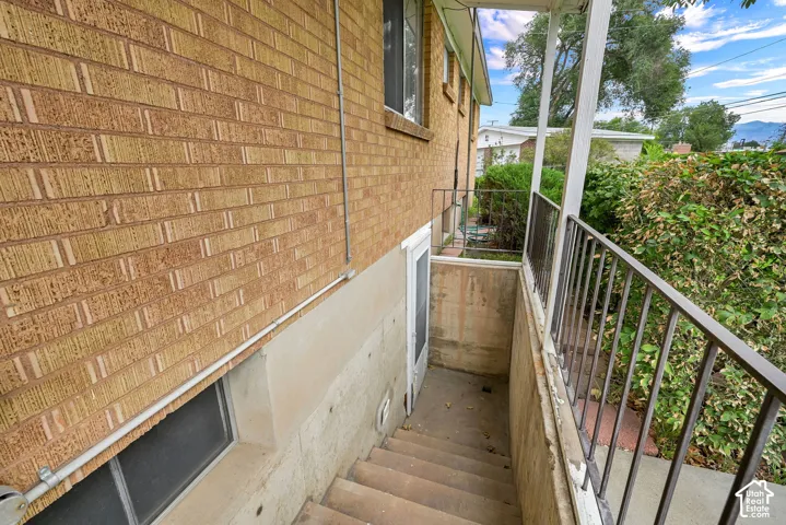 Brick exterior facade, exterior back basement staircase, metal handrail, lower-level entry, mature landscaping