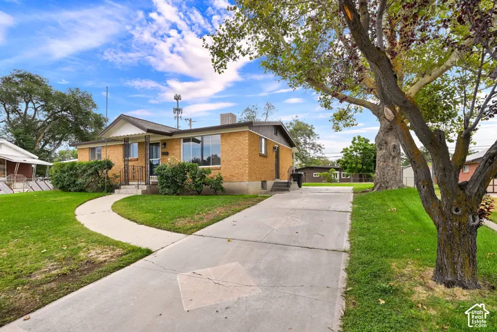 Brick exterior with a covered entry, established landscaping, concrete driveway, and a curved concrete pathway
