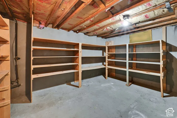 Unfinished basement space with concrete flooring, exposed ceiling joists, and extensive built-in wooden shelving units