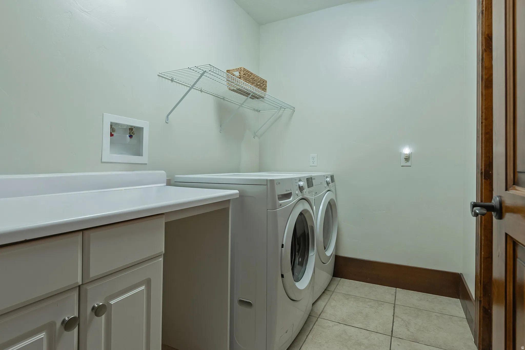 Laundry area with tile flooring, white cabinetry, a built-in countertop, and a wire shelving unit