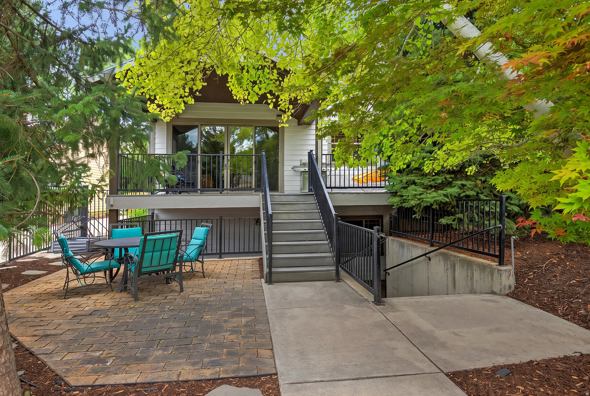 Patio with paver flooring, concrete pathway, exterior staircase, deck with sliding glass door, and black metal railings