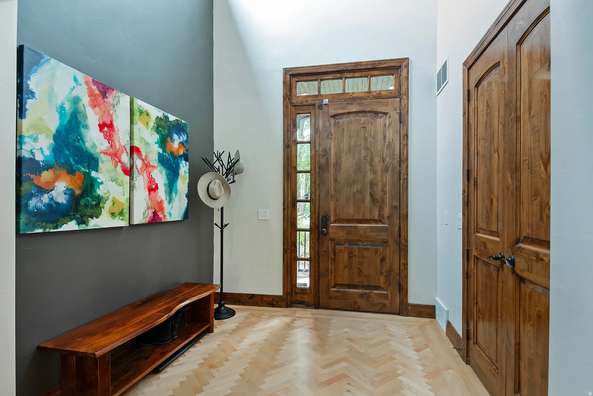 Herringbone wood-finish flooring, natural wood entry door with transom window, natural wood paneled closet doors, and a natural wood bench