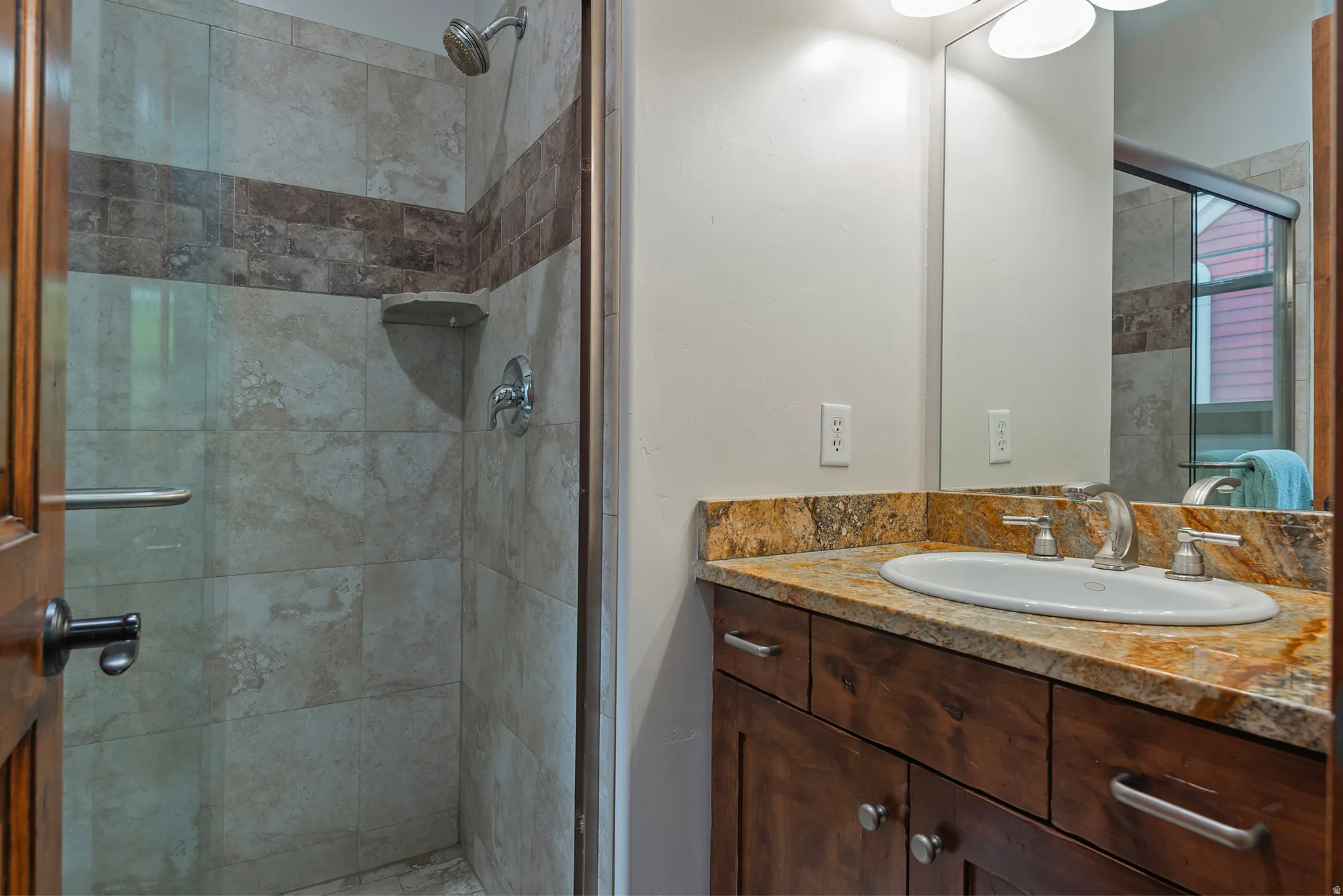 Wood-finish vanity with a built-in oval sink, stone countertop, and brushed nickel fixtures