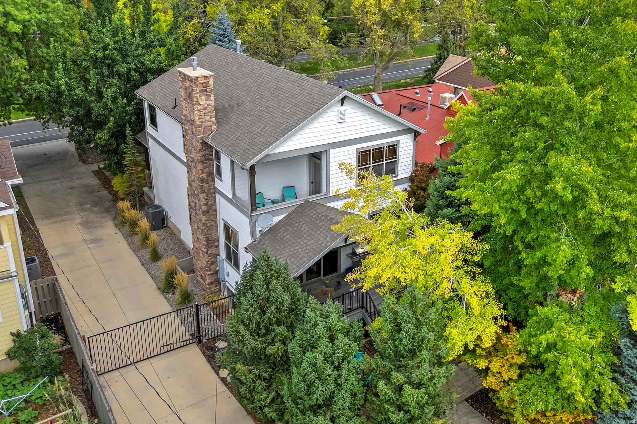 White siding exterior with a stone chimney, gray shingle roof, and an upper-level balcony