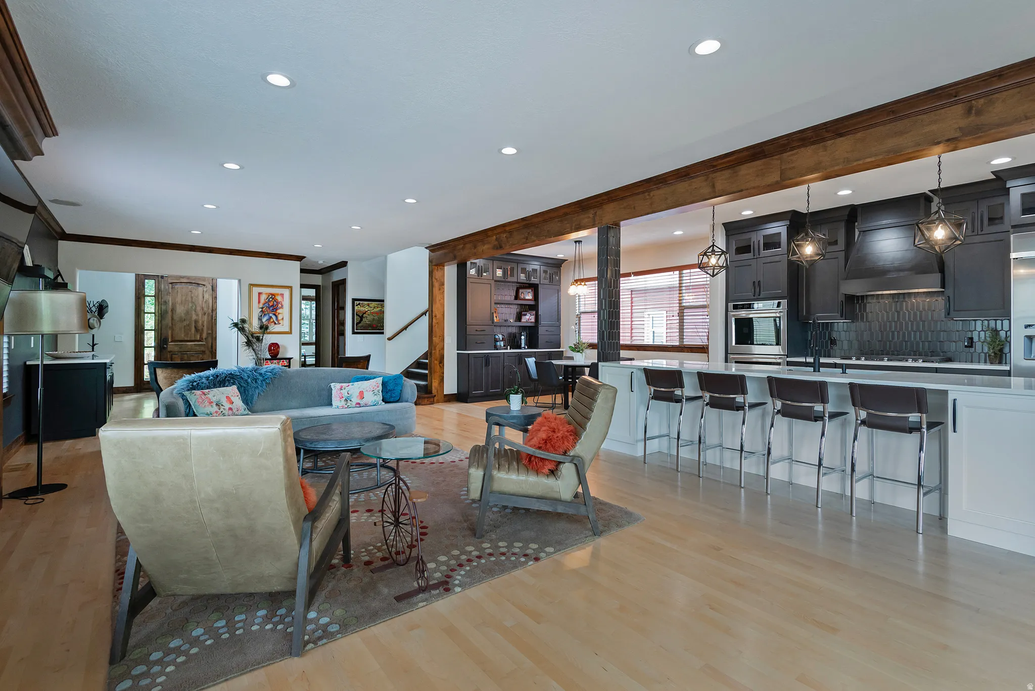 Open-concept living space featuring light wood-finish flooring, recessed lighting, and exposed wood beams