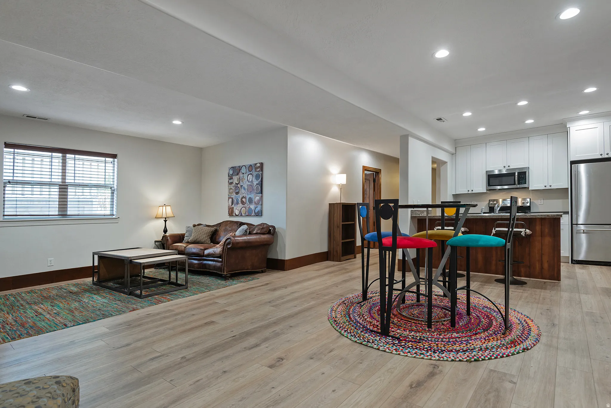 Recessed lighting throughout, wood-finish flooring, white cabinetry, stainless steel appliances, and a wood-finish island