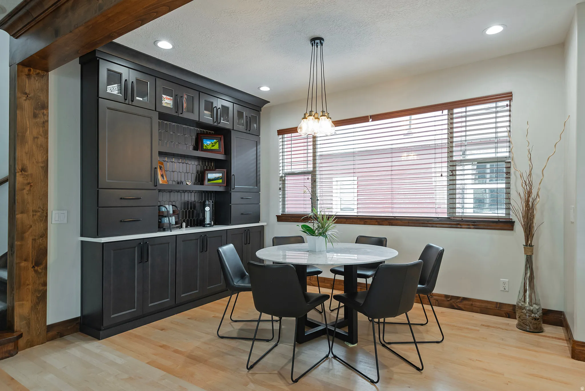 Built-in cabinetry with glass-front uppers and white countertop, wood-finish flooring, recessed lighting, and a window with wood trim