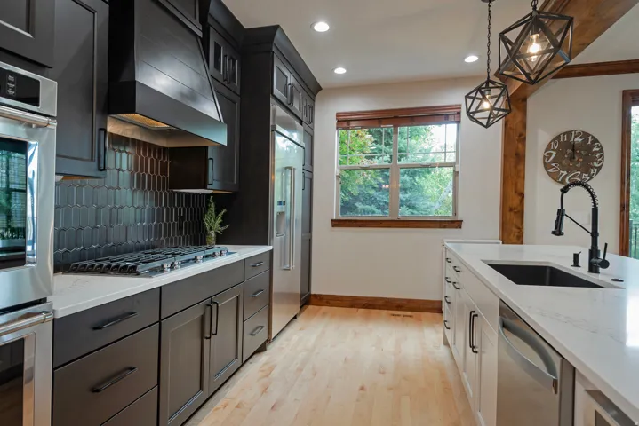 Gourmet kitchen featuring dark shaker-style cabinetry, stainless steel appliances, a tile backsplash, light wood-finish flooring, and pendant lighting