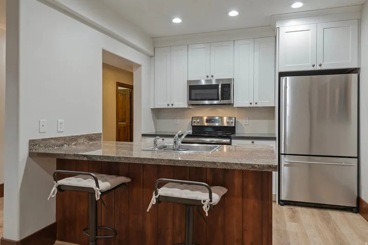 Kitchen featuring stainless steel appliances, upper white cabinetry, a built-in microwave, and a breakfast bar with a stone countertop