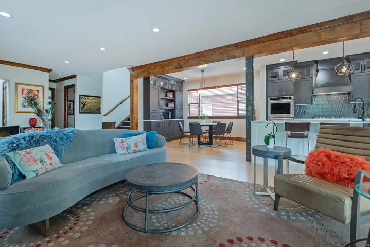 Open concept living area featuring wood-finish flooring, exposed beams, recessed lighting, and a kitchen with dark cabinetry, stainless steel appliances, and a tiled backsplash