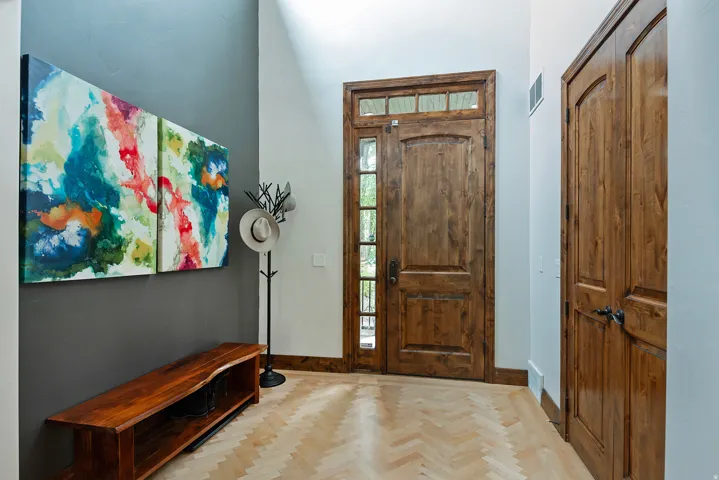 Herringbone wood-finish flooring, natural wood entry door with transom window, natural wood paneled closet doors, and a natural wood bench