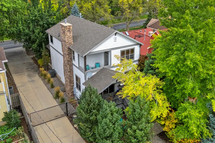 White siding exterior with a stone chimney, gray shingle roof, and an upper-level balcony