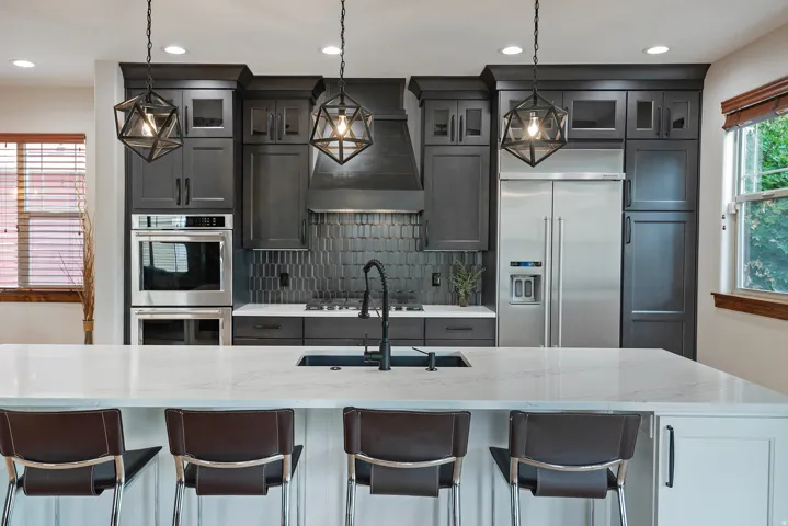 Kitchen featuring dark cabinetry, stainless steel appliances, a white island countertop, a black sink, and pendant lighting
