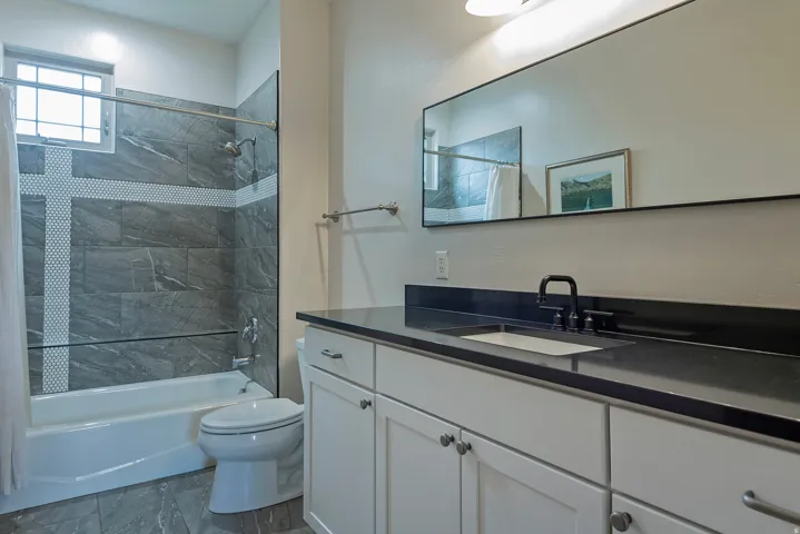 Full bathroom with a white tub and shower featuring gray tile with a mosaic accent