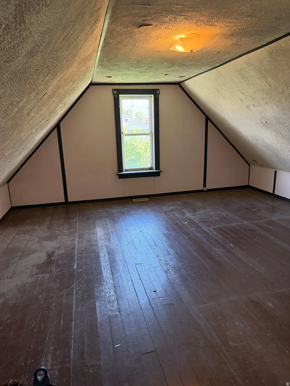 Attic space featuring wood-finish flooring, Two windows, an overhead light fixture, and sloped ceilings