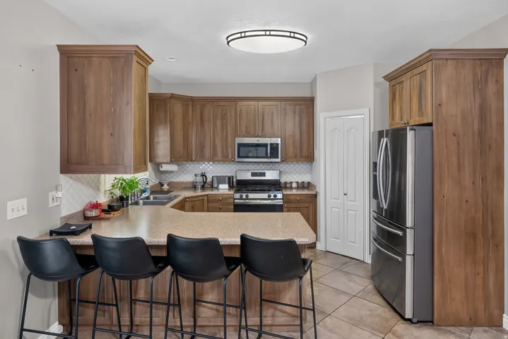 Wood-finish cabinetry, stainless steel appliances, breakfast bar, tile flooring, and a decorative tile backsplash