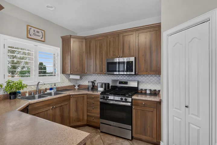 Kitchen featuring wood-finish cabinetry, stainless steel appliances, a double basin sink, and a tiled backsplash