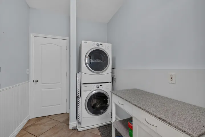 Laundry area featuring a built-in folding counter with a speckled countertop, tile flooring, and wainscoting
