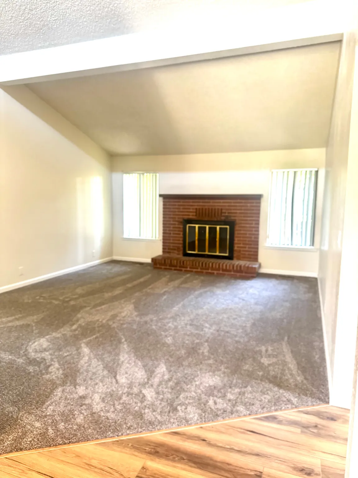 Vaulted ceiling with an exposed beam, brick fireplace with a brass firebox, carpet flooring, and wood-finish flooring