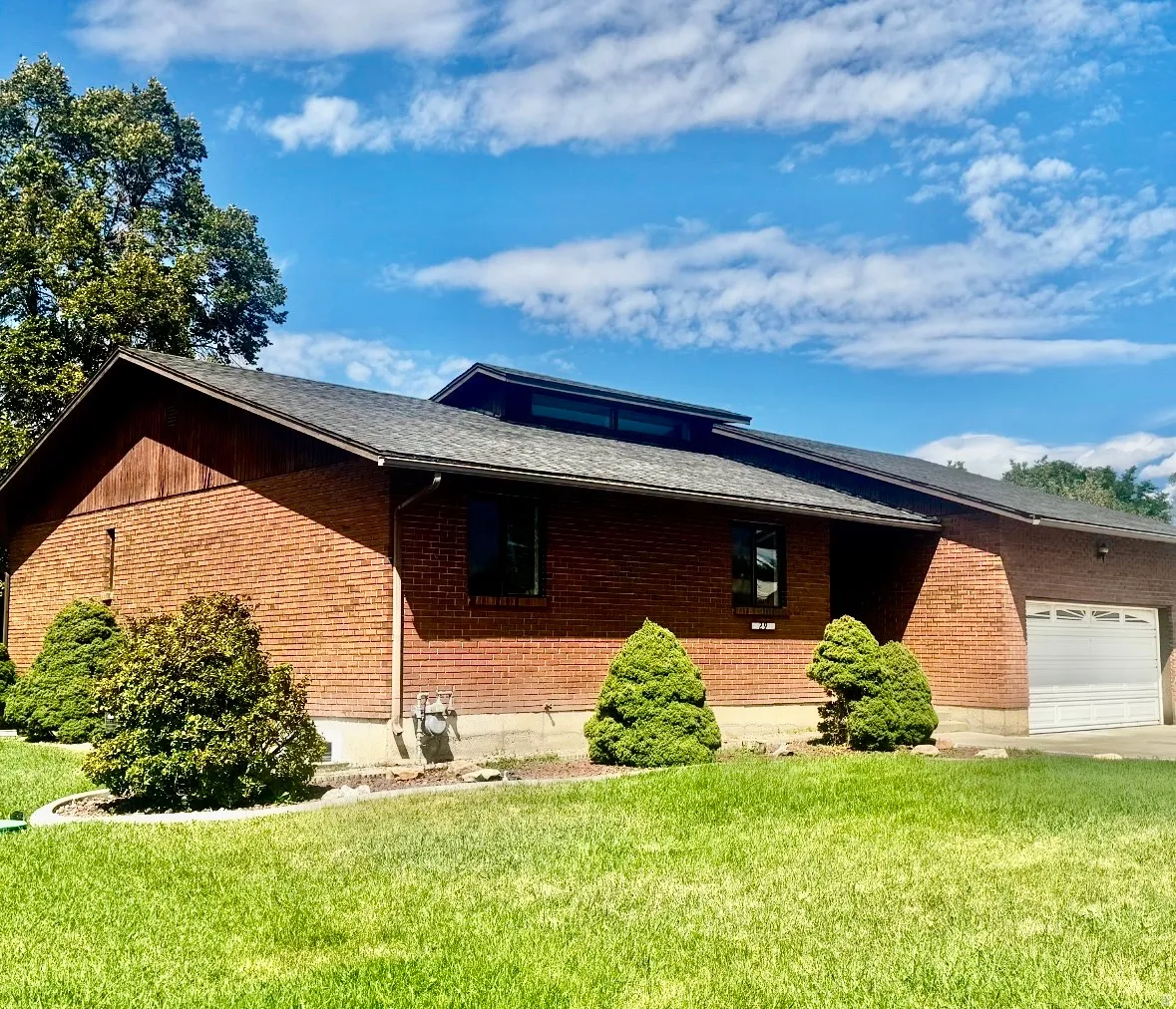 Charming brick ranch home featuring a clean, contemporary roofline with solar panels, attached two-car garage, and manicured landscaping with mature evergreen shrubs and established lawn