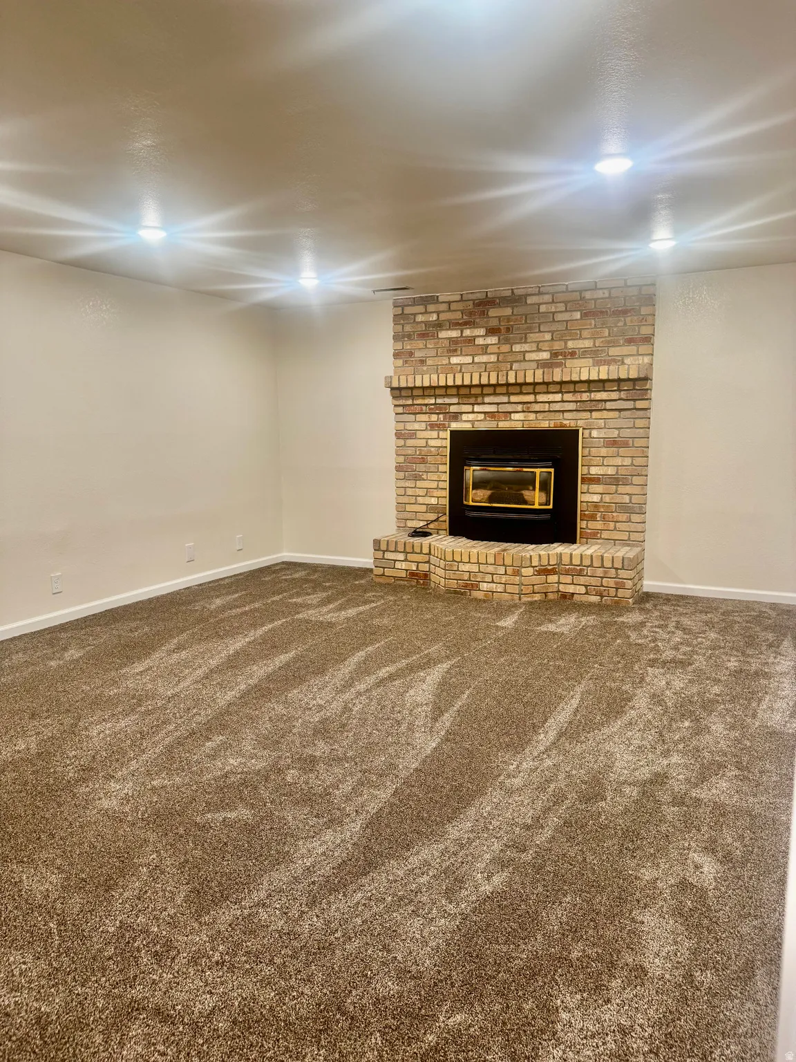 Recessed lighting, brick fireplace with a black insert, light-toned walls, and plush carpeting