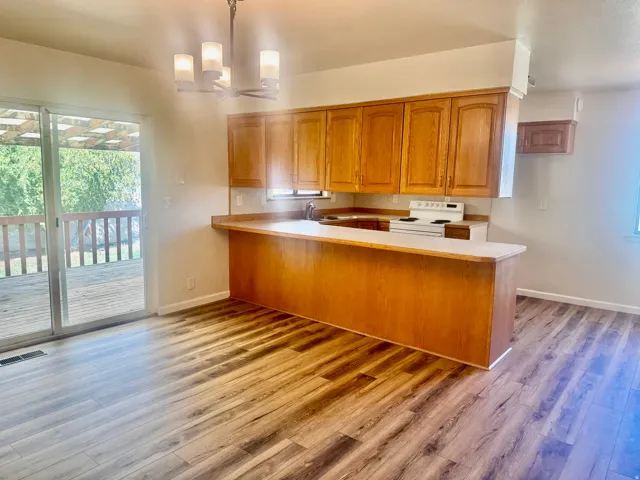 Wood-finish flooring, sliding glass door, wooden deck, wooden cabinetry, and a contemporary chandelier