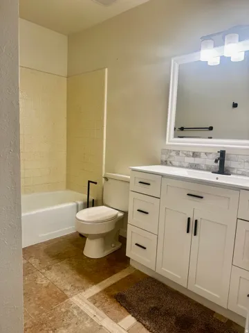 White vanity with black hardware, integrated sink, and a tiled backsplash