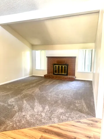 Vaulted ceiling with an exposed beam, brick fireplace with a brass firebox, carpet flooring, and wood-finish flooring