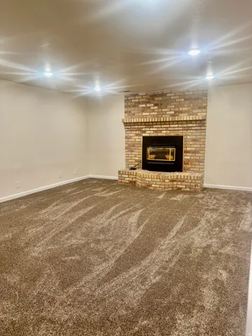 Recessed lighting, brick fireplace with a black insert, light-toned walls, and plush carpeting