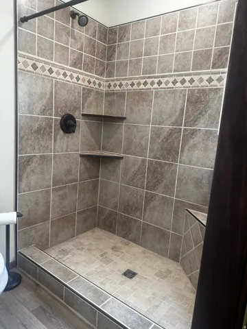 Tiled shower enclosure featuring a decorative accent band, integrated corner shelves, and a dark bronze shower head and controls