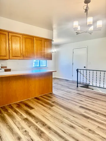 Wood-finish flooring, wood cabinetry, white countertops, built-in breakfast bar, and contemporary chandelier lighting
