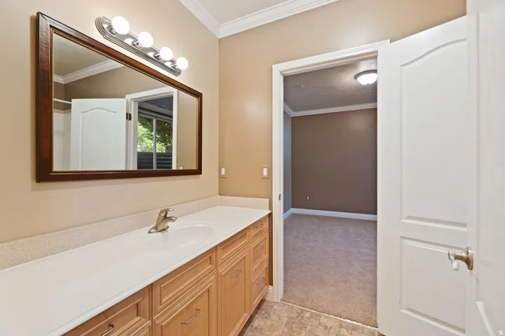 Extended vanity with integrated sink, wood-finish cabinetry, a framed mirror, and crown molding