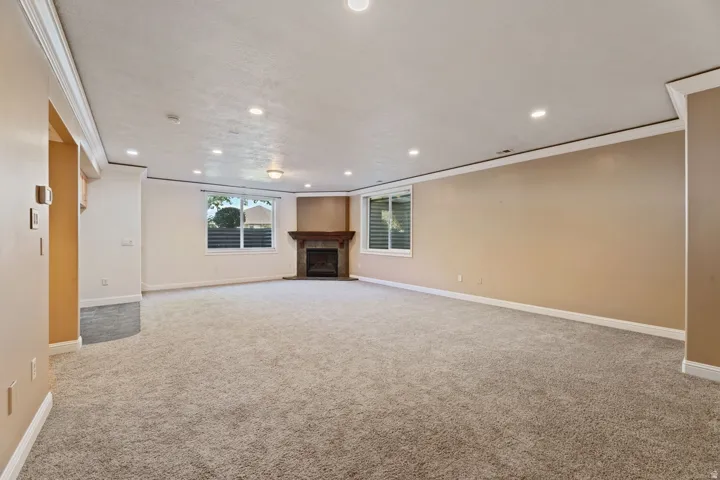 Spacious room featuring carpeting, a corner fireplace with a wood mantel, multiple windows, and recessed lighting