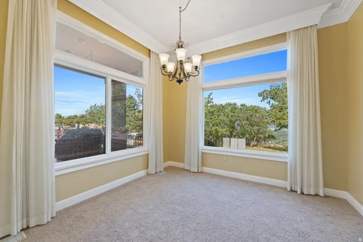 Expansive window openings with white trim, crown molding, a hanging light fixture, and neutral-toned carpeting