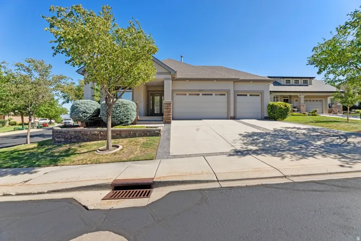 Stucco exterior with stone accents, a three-car garage, concrete driveway, and front landscaping featuring mature trees and shrubbery