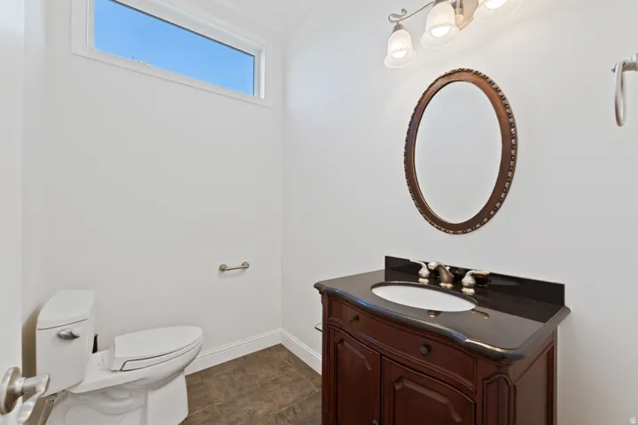 Powder room featuring a dark wood-finish vanity with an undermount sink, a dark stone countertop, an ornate framed mirror, and a transom window