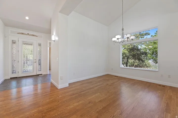 Vaulted ceiling, hardwood flooring, large picture window, decorative double entry doors with sidelights, and a chandelier