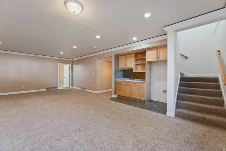 Carpeted living area featuring recessed lighting, a built-in wet bar with wood cabinetry, and an open staircase with a wood handrail