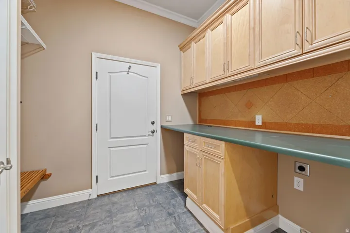 Laundry area featuring upper and lower cabinetry, an extended countertop, a decorative backsplash, and durable tile flooring