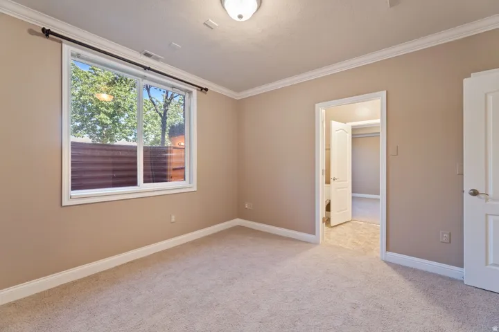Carpeted room with a large window, crown molding, and a paneled door