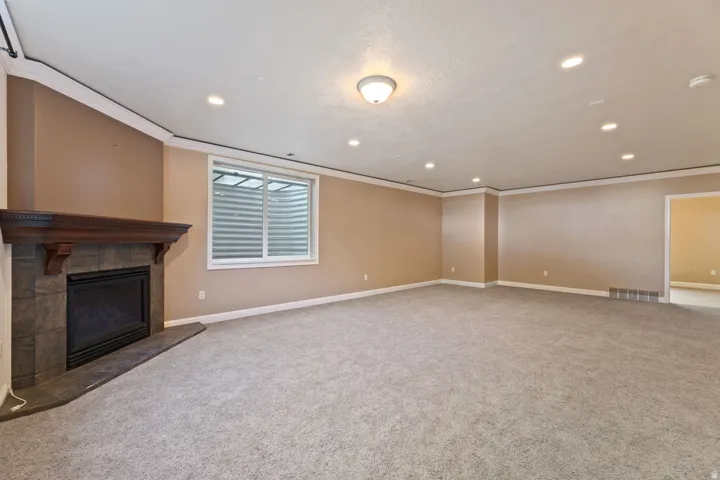 Spacious room featuring a corner fireplace with a dark wood mantel and stone surround, recessed lighting, crown molding, and light-toned carpeting