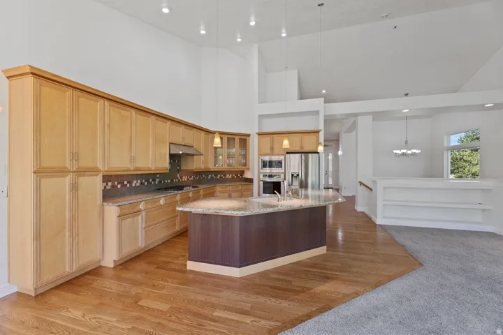 Kitchen featuring light wood cabinetry, a central island with a granite countertop, stainless steel appliances, and wood-finish flooring