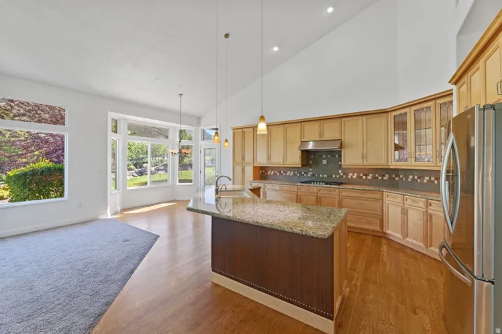 High vaulted ceilings, abundant natural light, wood-finish flooring, central kitchen island with stone countertop, and stainless steel appliances