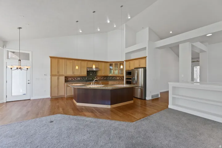 Vaulted ceilings with recessed lighting, wood-finish flooring, a kitchen island with stone countertops, stainless steel appliances, and built-in shelving