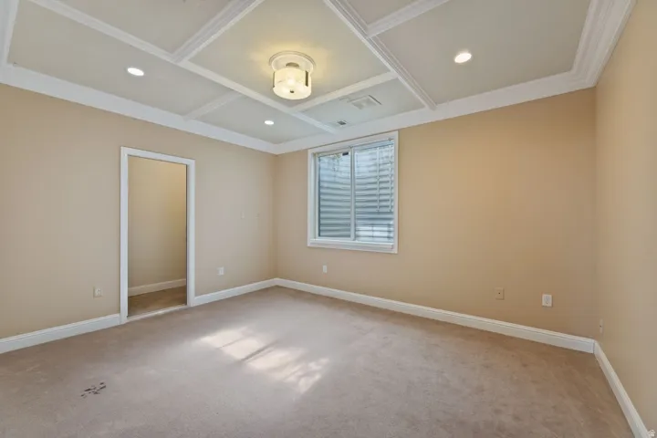 Coffered ceiling with recessed lighting and a central flush-mount fixture, neutral wall tones, and carpet flooring