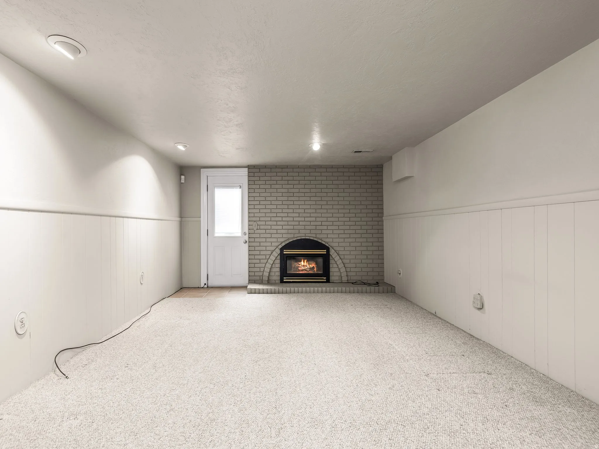Light-colored carpeting, white wainscoting, recessed lighting, brick fireplace, and a glass-paneled door