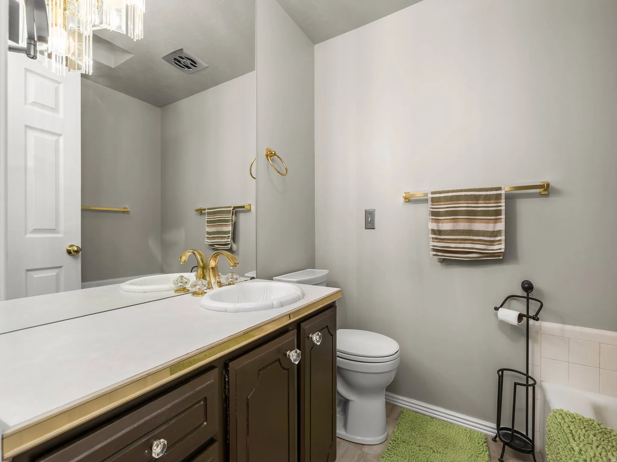 Elegant bathroom featuring a dark wood vanity with white countertop and round vessel sink, brass hardware and fixtures, large framed mirror, and tile flooring