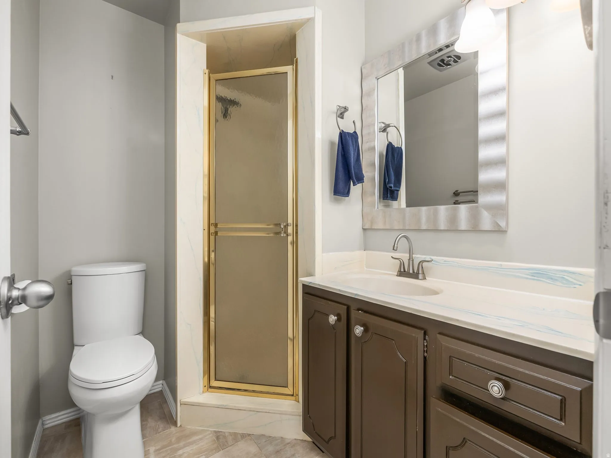 Spa-inspired bathroom featuring a wood-finish vanity with ample storage, white quartz countertop, chrome widespread faucet, and large framed mirror with integrated lighting